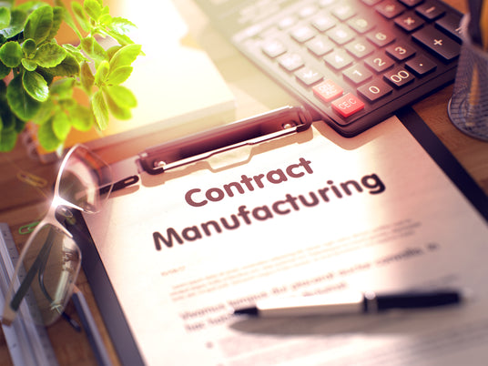 Contract manufacturing document surrounded by a pen, calculator and small plant.
